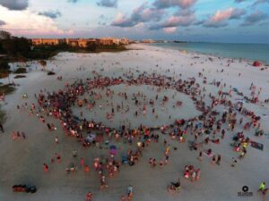 Aerial view of the Siesta Key Drum Circle with a large crowd gathered in a circle on the beach at sunset
