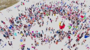 "Aerial view of the Siesta Key Drum Circle with crowds gathered on the beach at sunset"