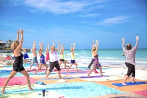 Group of people practicing yoga on colorful mats at Siesta Key Beach with the Gulf of Mexico in the background.