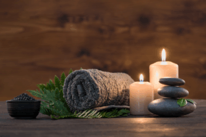 Spa setup with rolled towel, lit candles, smooth stacked stones, and green leaves creating a relaxing atmosphere.