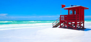Red lifeguard stand on Siesta Key Beach with turquoise Gulf waters and clear blue skies.