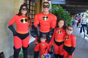A family dressed as The Incredibles poses together during the Siesta Key Safe Treats event, smiling in matching red superhero costumes while holding trick-or-treat bags.