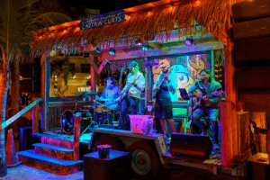 Nighttime scene of a tropical outdoor bar and music venue with a band on a small stage.