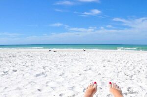 Relaxing on Siesta Key Beach with white quartz sand and turquoise Gulf waters under a clear blue sky.