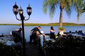 Guests enjoying waterfront dining at an outdoor restaurant in Siesta Key, Florida, with palm trees and bay views.