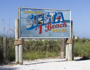 Sign at Siesta Beach in Sarasota, Florida, reading “Siesta Beach #1 in the USA!” with a beach background and wooden posts wrapped in rope.
