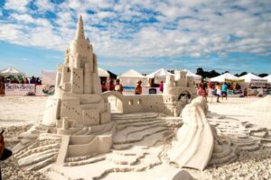Intricate castle-themed sand sculpture displayed at the Siesta Key Crystal Classic with festival tents and visitors in the background.
