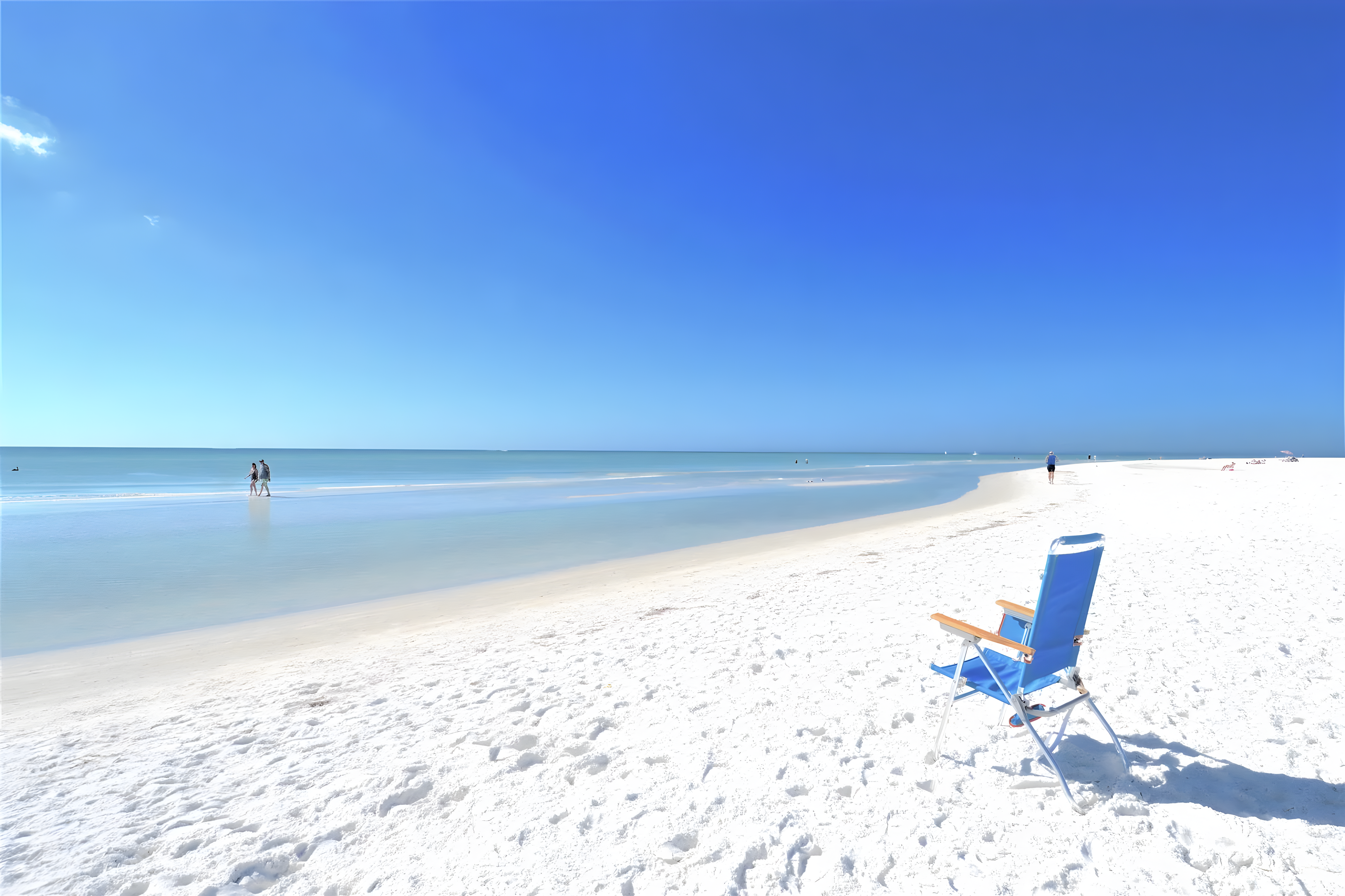 Bright white sand and calm turquoise water at Siesta Key Beach under a clear blue sky, with a blue beach chair in the foreground.