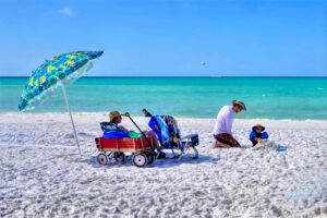 Family relaxing on Siesta Key Beach under a colorful umbrella, with white sand and turquoise Gulf water.