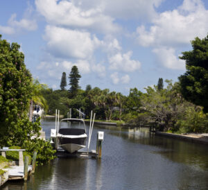Boat on a private lift along a calm residential canal in Siesta Key, surrounded by tropical trees and waterfront homes under a partly cloudy sky
