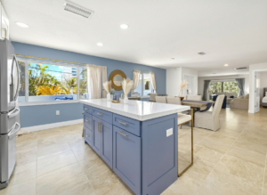 Modern kitchen and dining area Open-concept kitchen with blue island, white countertops, and dining area, featuring large windows and bright natural light