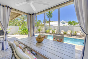 Outdoor patio with dining table overlooking private pool at Siesta Key vacation rental, surrounded by palm trees and tropical landscaping
