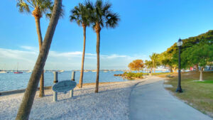 Bayfront Park in Siesta Key featuring a waterfront gazebo, palm trees, and a landscaped garden with a park sign in the foreground under a clear sunny sky.