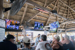 Customers watching football games inside The Big Tiki Lounge in Siesta Key, Florida, with multiple TVs, tiki-style seating, and a lively sports bar atmosphere.