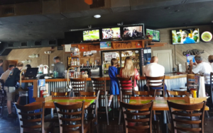 Fans watching football inside MVP – My Village Pub in Siesta Key, featuring multiple TVs, tiki-style seating, and a lively sports bar atmosphere.