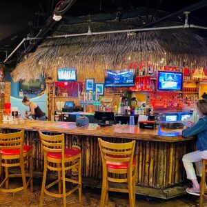 Interior of Gilligan’s Island Bar & Grill in Siesta Key featuring a tiki-style bar, sports playing on TVs, bamboo decor, and casual island bar seating.