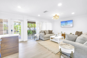 Bright living room inside a Siesta Key vacation rental featuring comfortable seating, a large TV for watching sports and games, and sliding doors leading to a tropical outdoor patio.