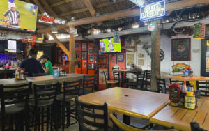 Interior of Siesta Key Oyster Bar (SKOB) with football games playing on TVs, wooden tables, neon beer signs, and a casual sports bar atmosphere in Siesta Key Village.