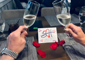 Couple toasting with champagne during a romantic anniversary dinner in Siesta Key, with rose petals and a personalized celebration card on the table.