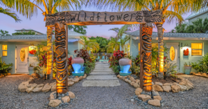 The Wildflower by Gertrude Rentals on Siesta Key, featuring tropical landscaping, a carved wooden entrance, and colorful courtyard lighting.
